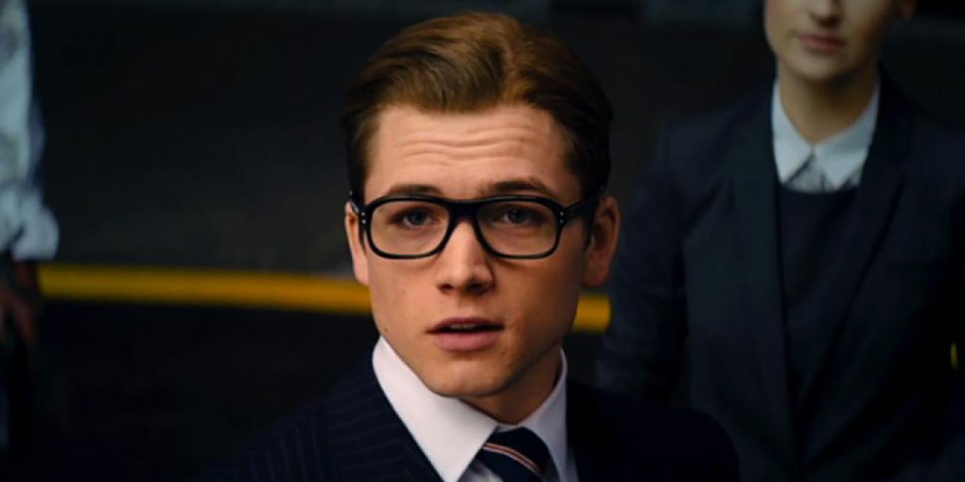 Taron Egerton in The Kingsman: The Secret Service wearing a suit and tie and dark-rimmed glasses.