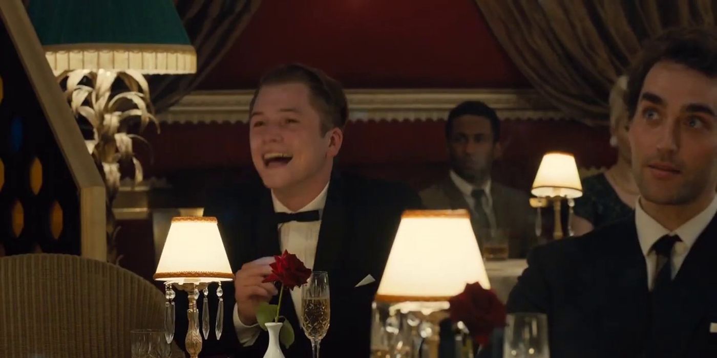 Taron Egerton in a suit and bowtie, sitting in a restaurant laughing in a scene from Legend.