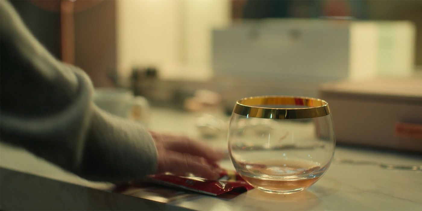 Molly's hand reaching for a gold-rimmed glass in her home on Loot.