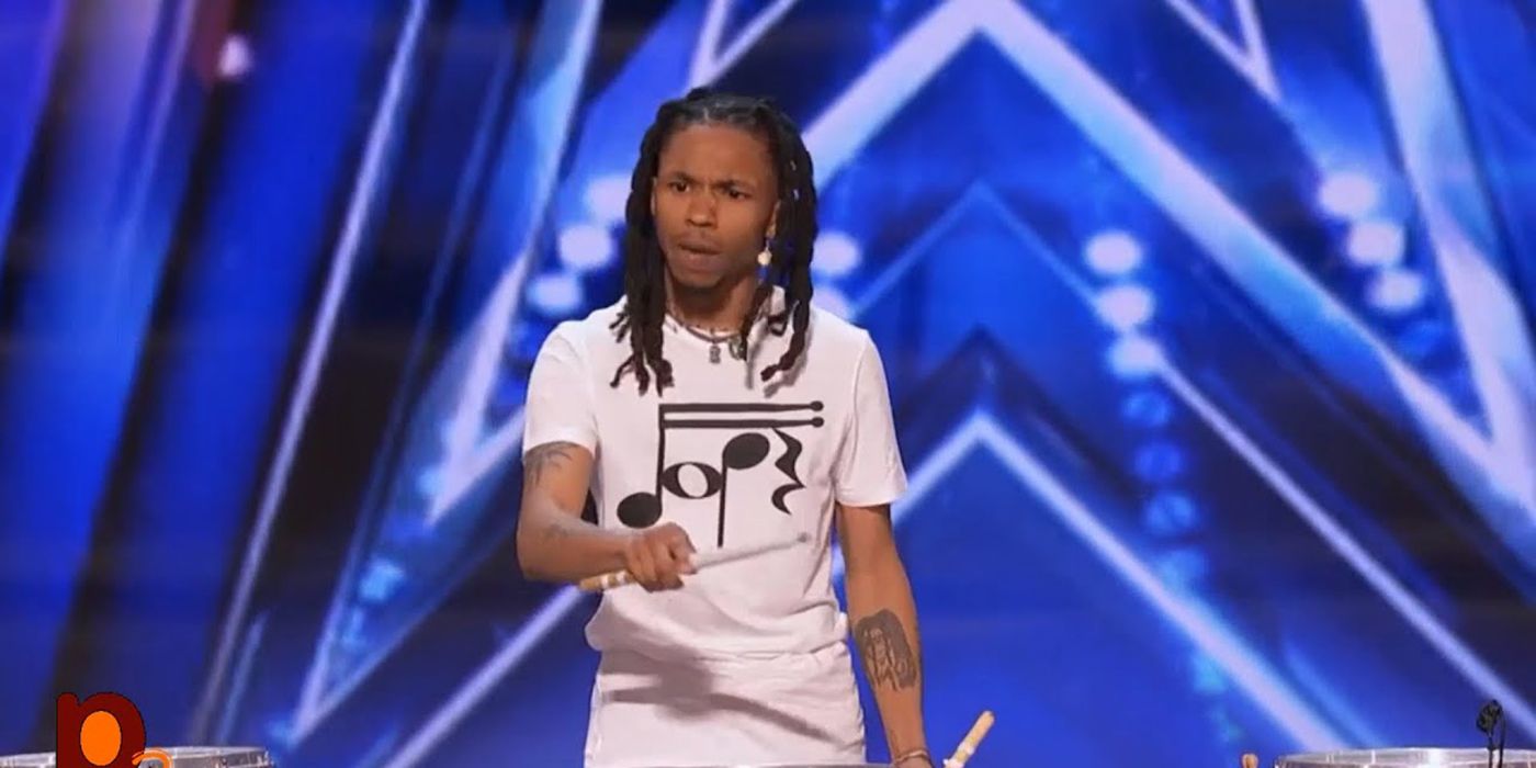 Malik Dope on stage on AGT, holding drumsticks ready to play.
