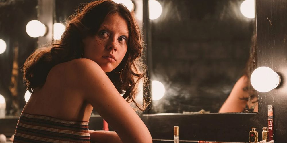Maxine sits at the makeup mirror in X