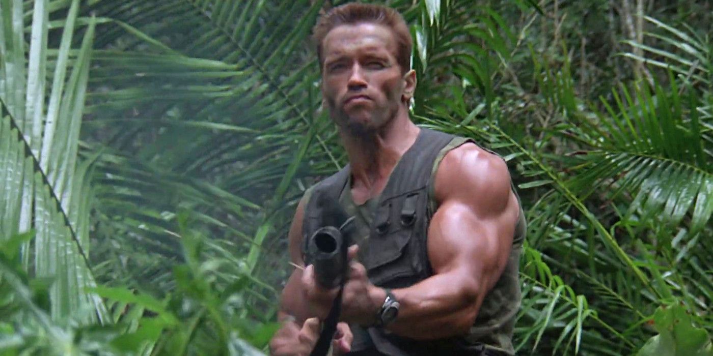 Arnold Schwarzenegger como Dutch em Predator apontando uma metralhadora enquanto está em frente à folhagem da selva