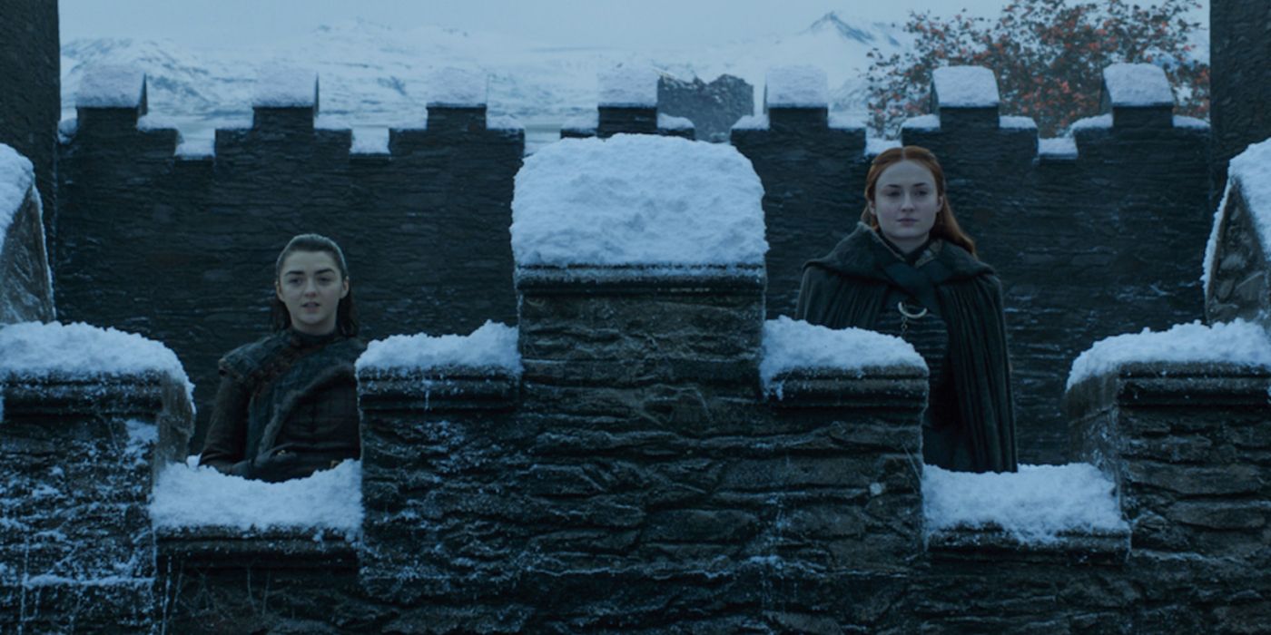 Arya and Sansa standing together at the snowy fortress of Winterfell.