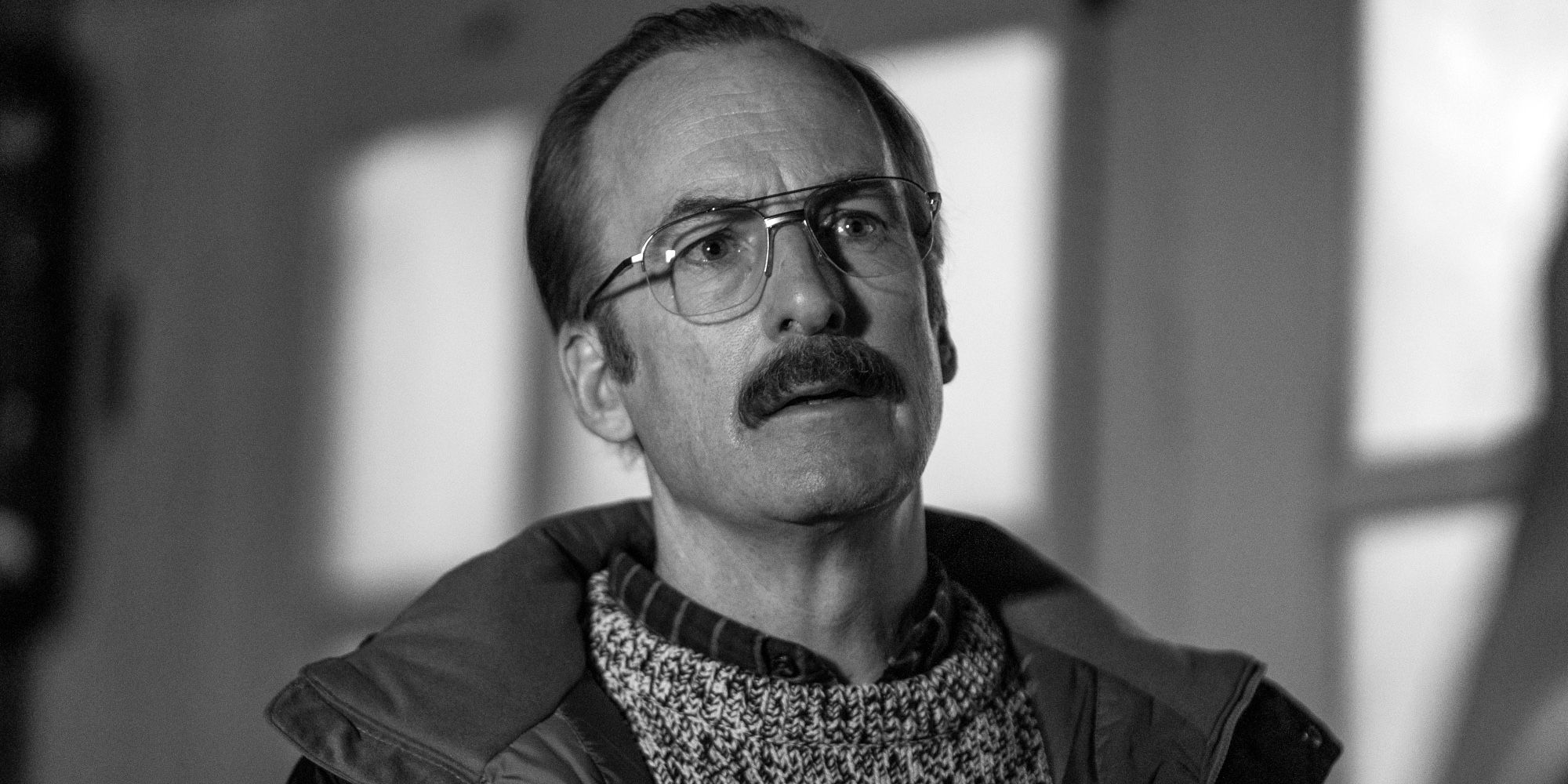 Gene em Better Call Saul em preto e branco, com bigode e óculos, parecendo assustado.