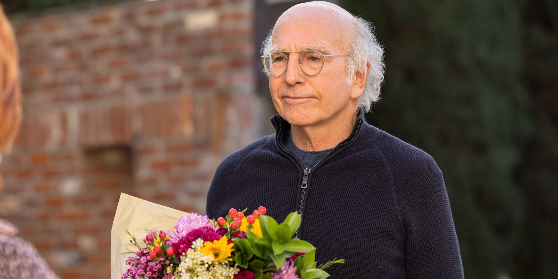 Larry David looking annoyed while holding flowers in Curb Your Enthusiasm season 11