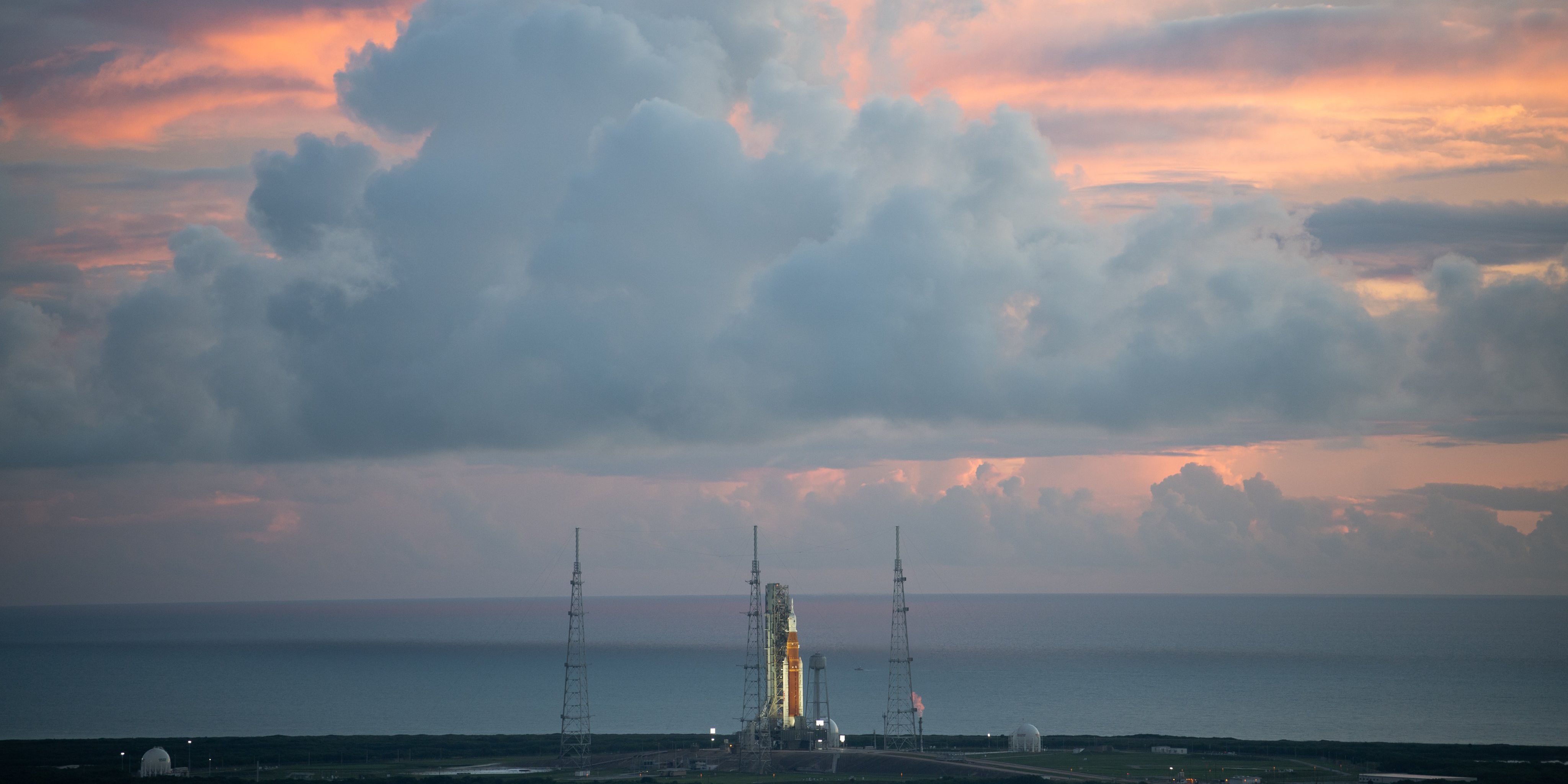 The SLS rocket on the launch pad from a distance against the dawn sky.