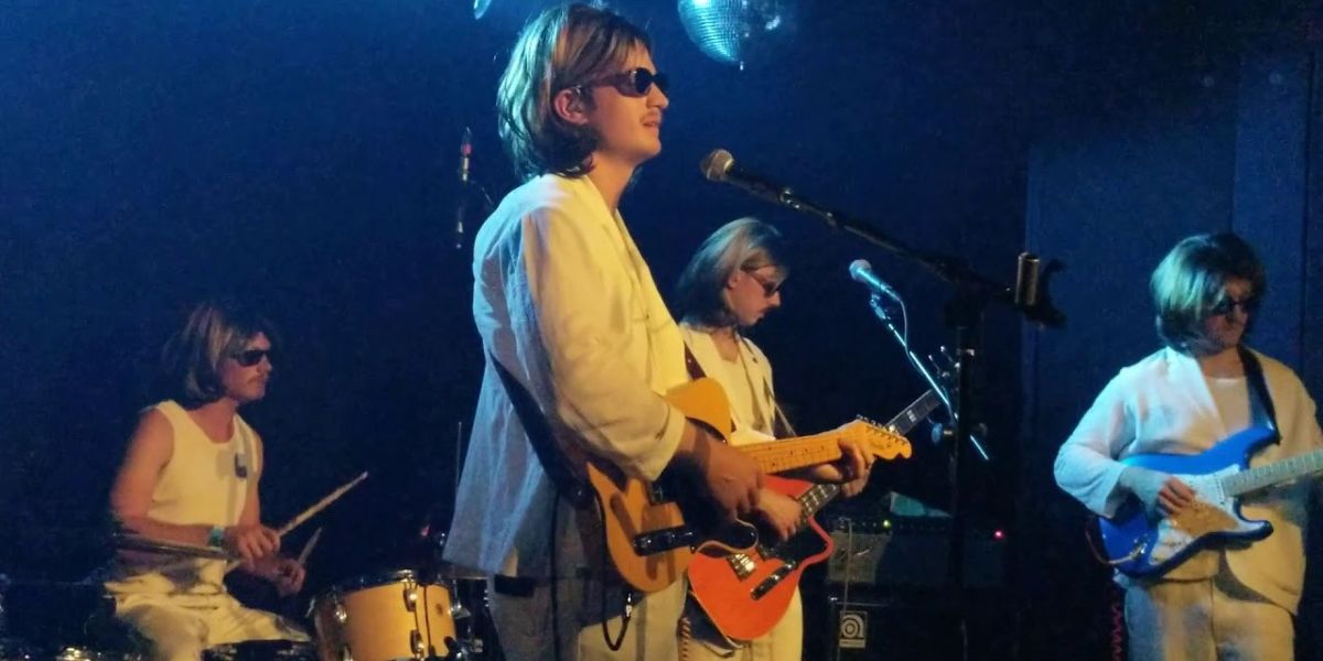 Joe Keery playing guitar onstage in a white suit