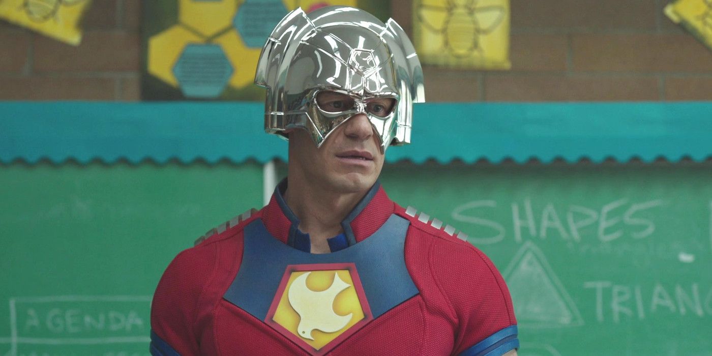 John Cena in character as Peacemaker in Peacemaker wearing a silly silver helmet in a school classroom and looking sad
