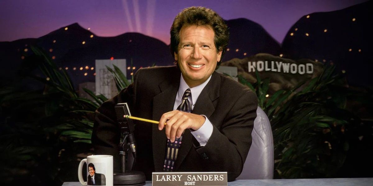 Larry sentado em sua mesa no The Larry Sanders Show