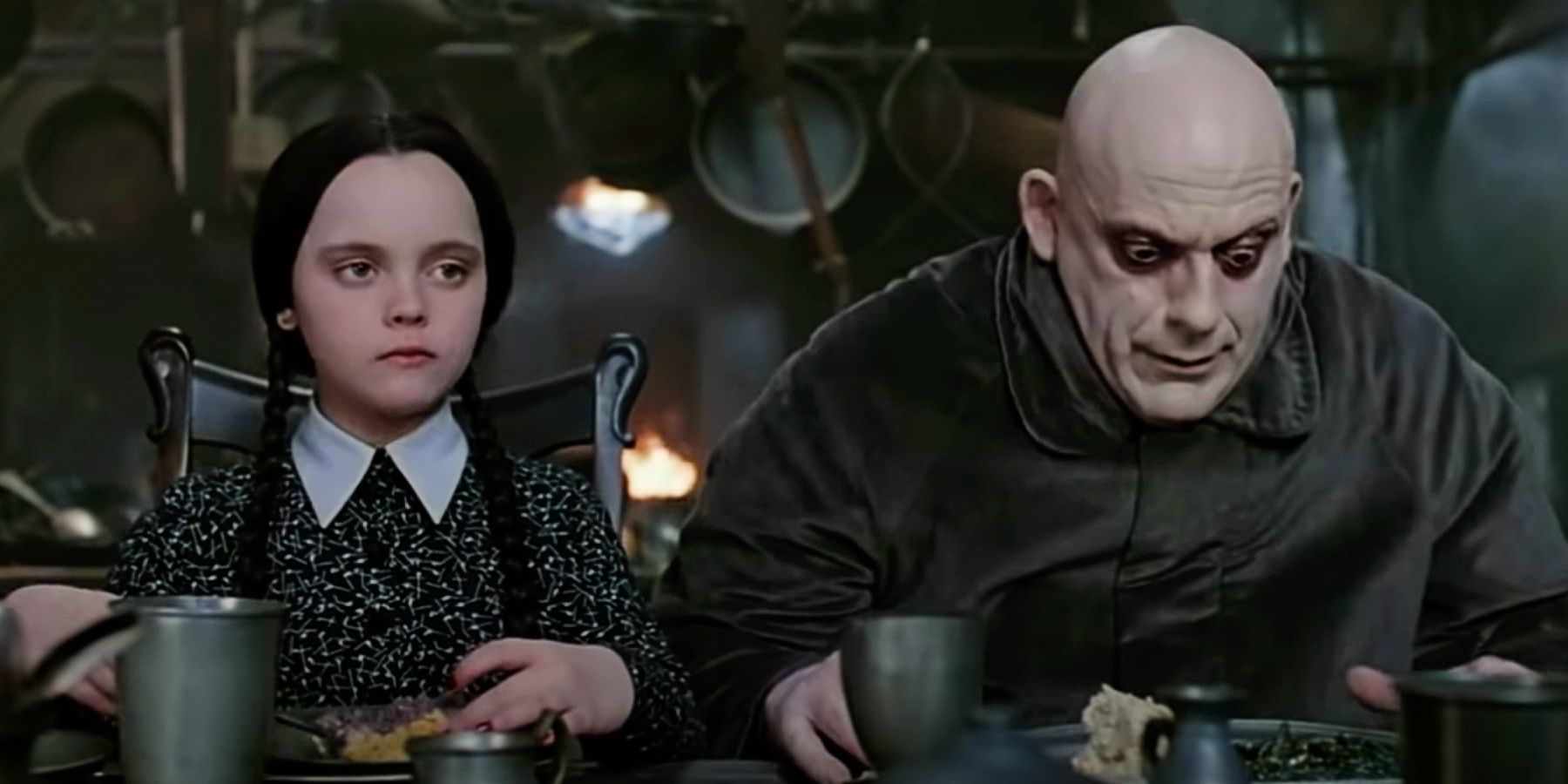 A Família Addams Christina Ricci como Wednesday e Christopher Lloyd como Tio Fester sentados em uma mesa