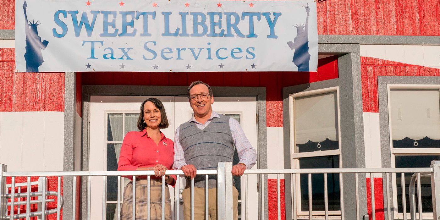 An average-looking middle-aged man-and-woman couple stand smiling in front of a crudely painted building under a sign reading Sweet Liberty Tax Services