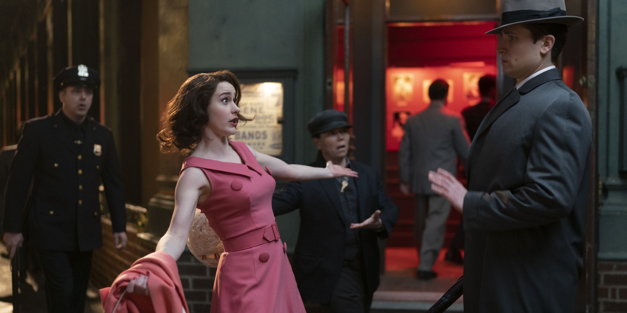 Midge Maisel from The Marvelous Mrs. Maisel, arms outstretched speaking to a man, Susie in the background.