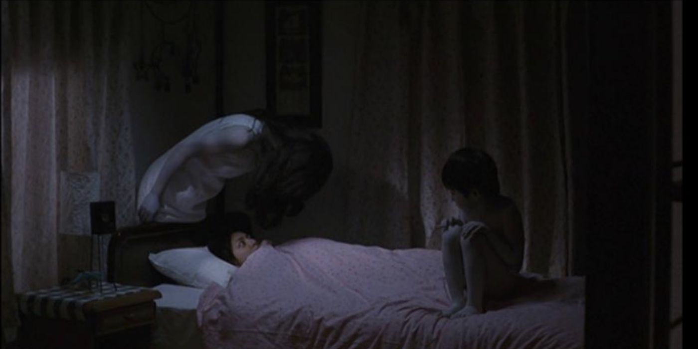 A woman in bed being haunted by two ghosts in Ju On: The Grudge