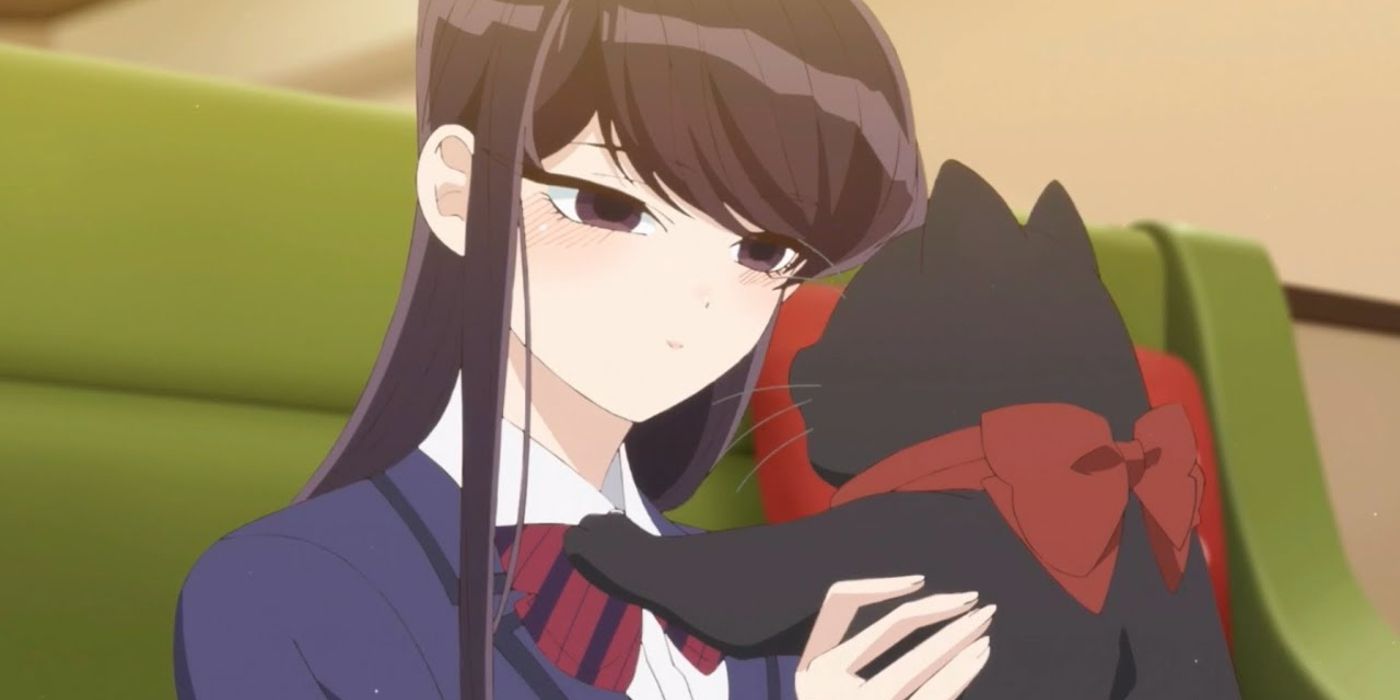 Image of Komi holding up a big black cat with a red ribbon round its neck