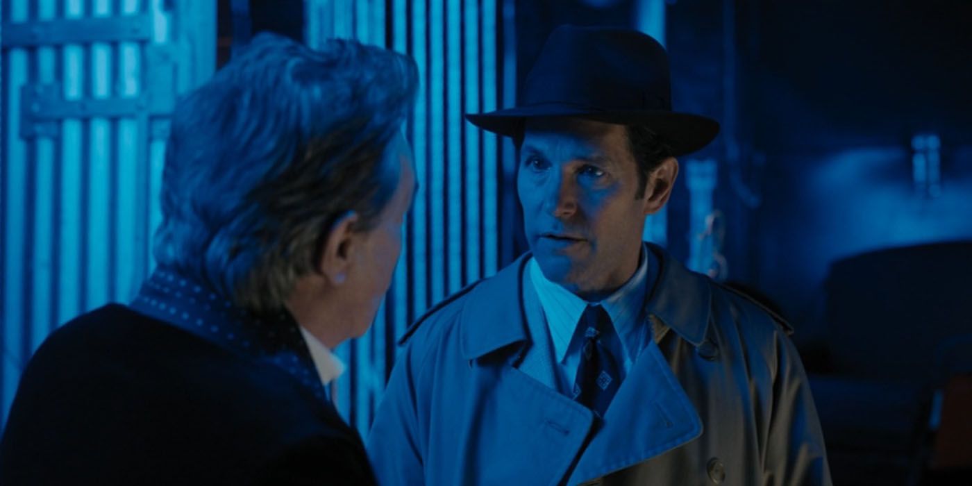 Paul Rudd in a raincoat and hat on a dark blue lit background talking to Oliver in a scene from Only Murders in the Building.