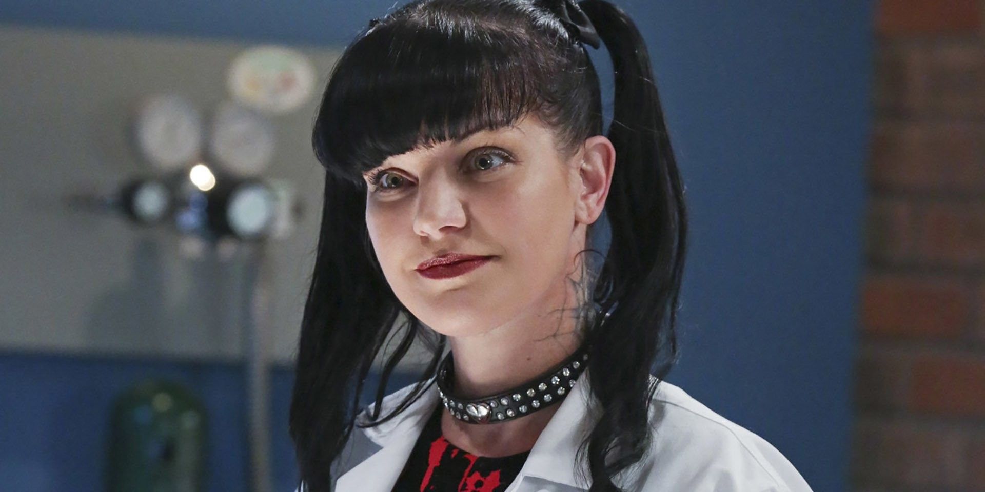 Abby Scuito (Pauley Perrette), wearing a labcoat and leather choker, smiles in the lab from NCIS