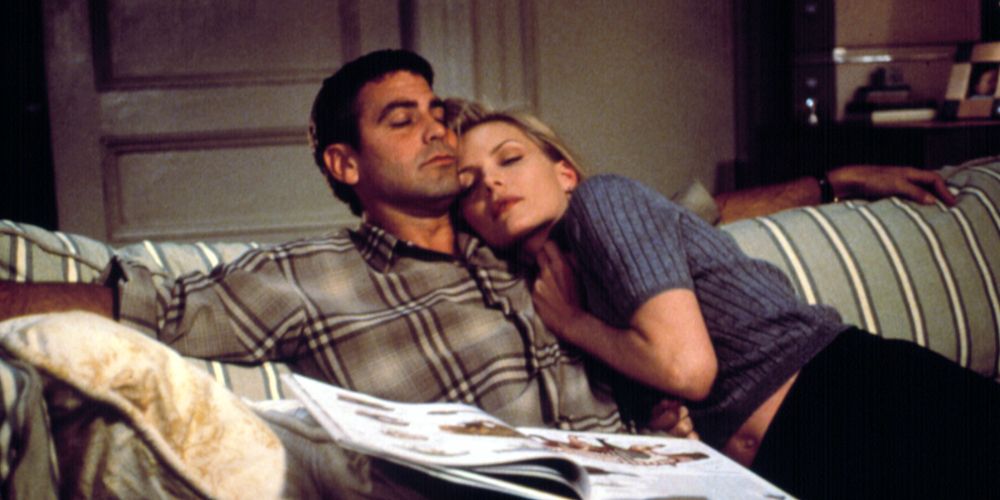 An image of George Clooney and Michelle Pfeiffer sitting together on the couch in One Fine Day