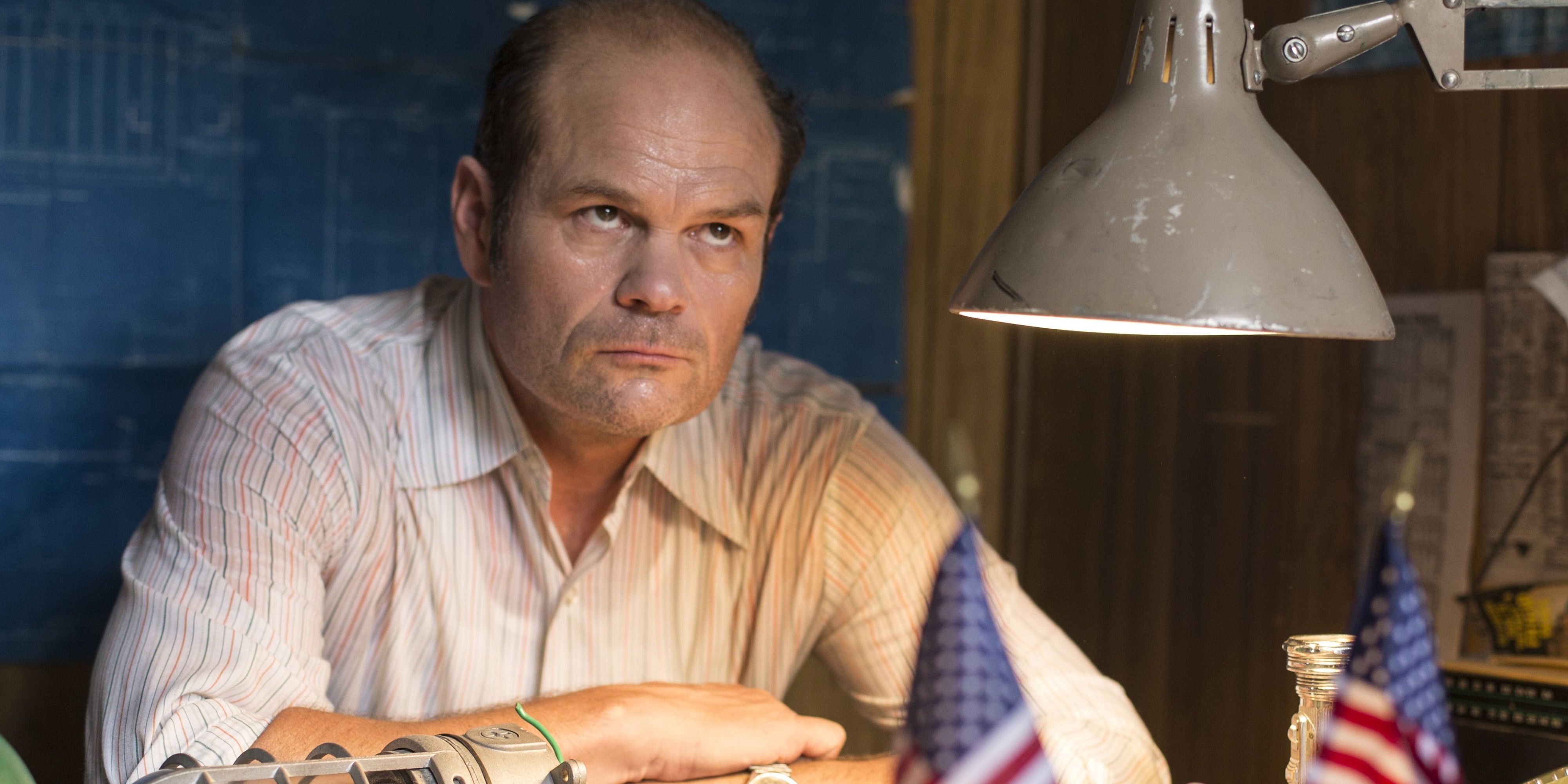Chris Bauer sitting at a table with arms crossed in The Deuce Cropped