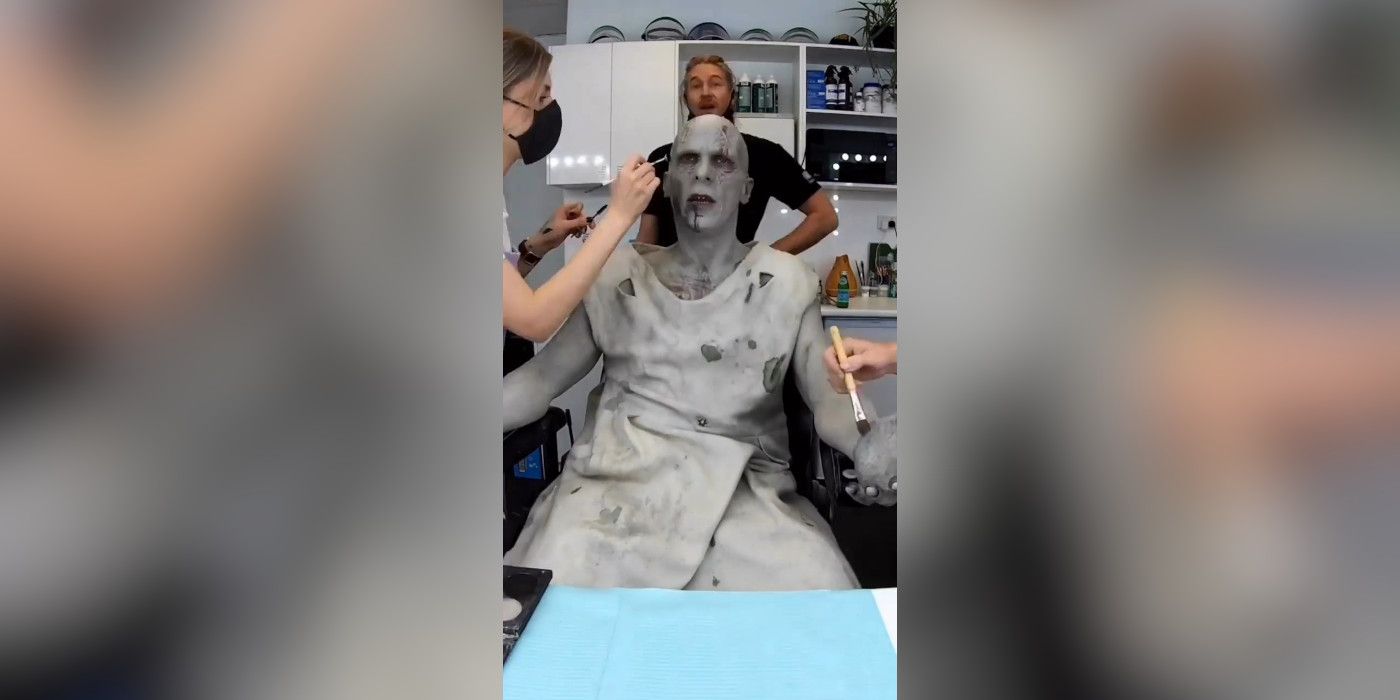 Actor Christian Bale sits in a makeup chair being transformed by several makeup artists into Gorr the God Butcher