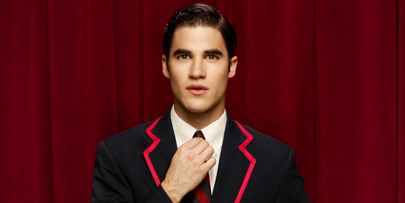 Darren Criss Glee poses in front of a red curtain