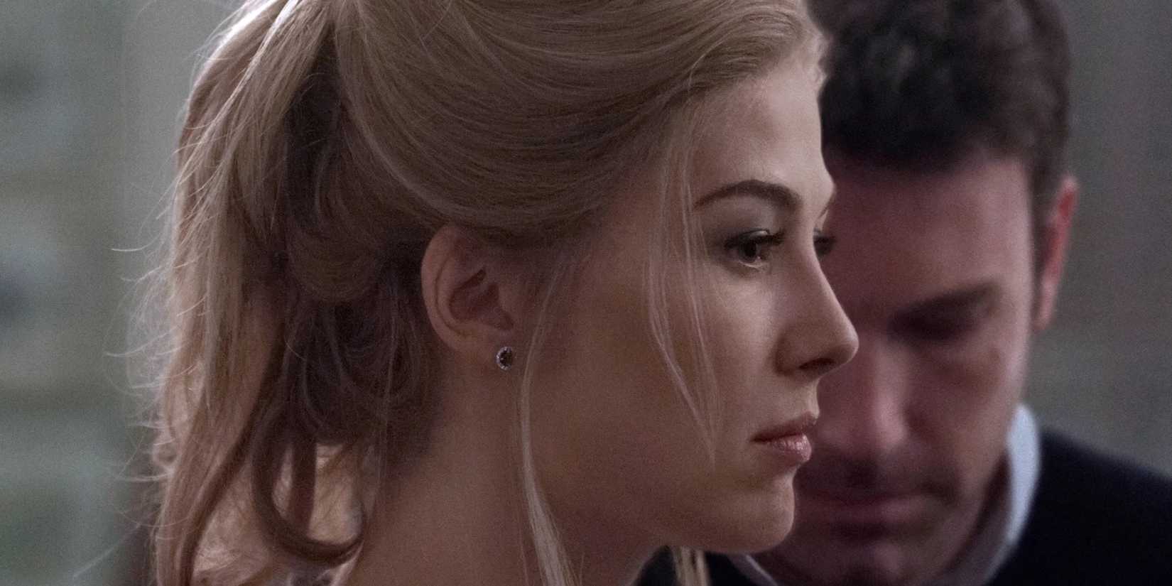Rosamund Pike as Amy Dunne looking sad as Ben Affleck as Nick Dunne hangs his head in Gone Girl (2014)