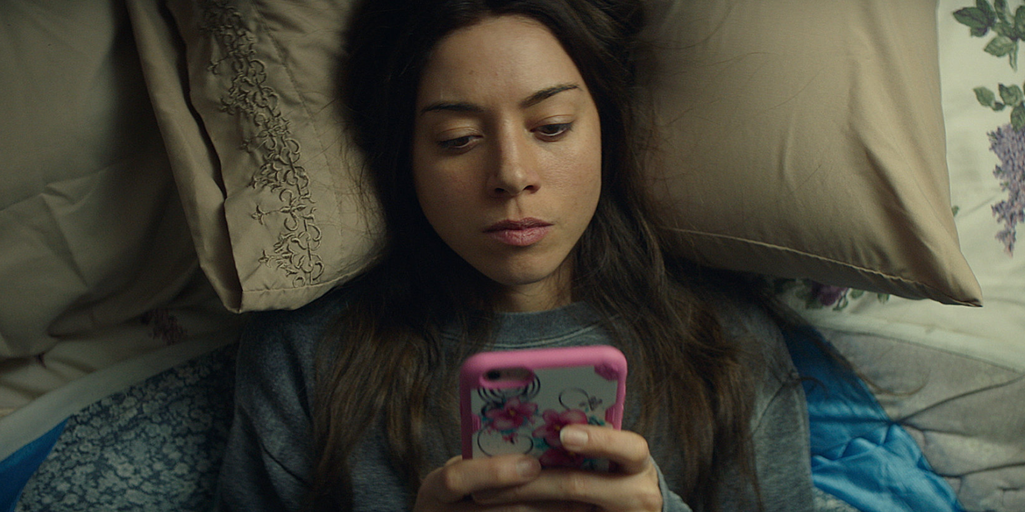 Ingrid (Aubrey Plaza) lies on her bed and is on her phone in Ingrid Goes West.