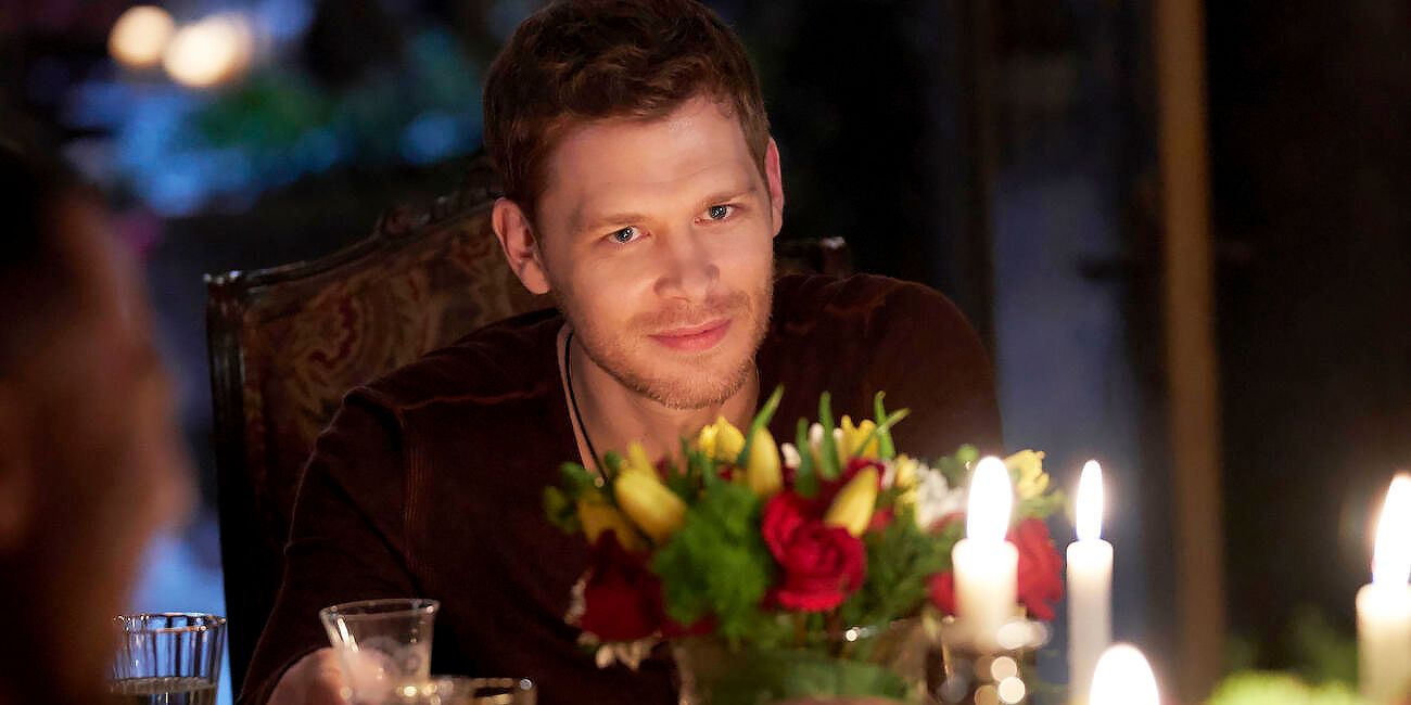 Klaus en The Originals sentado detrás de una mesa y sonriendo.