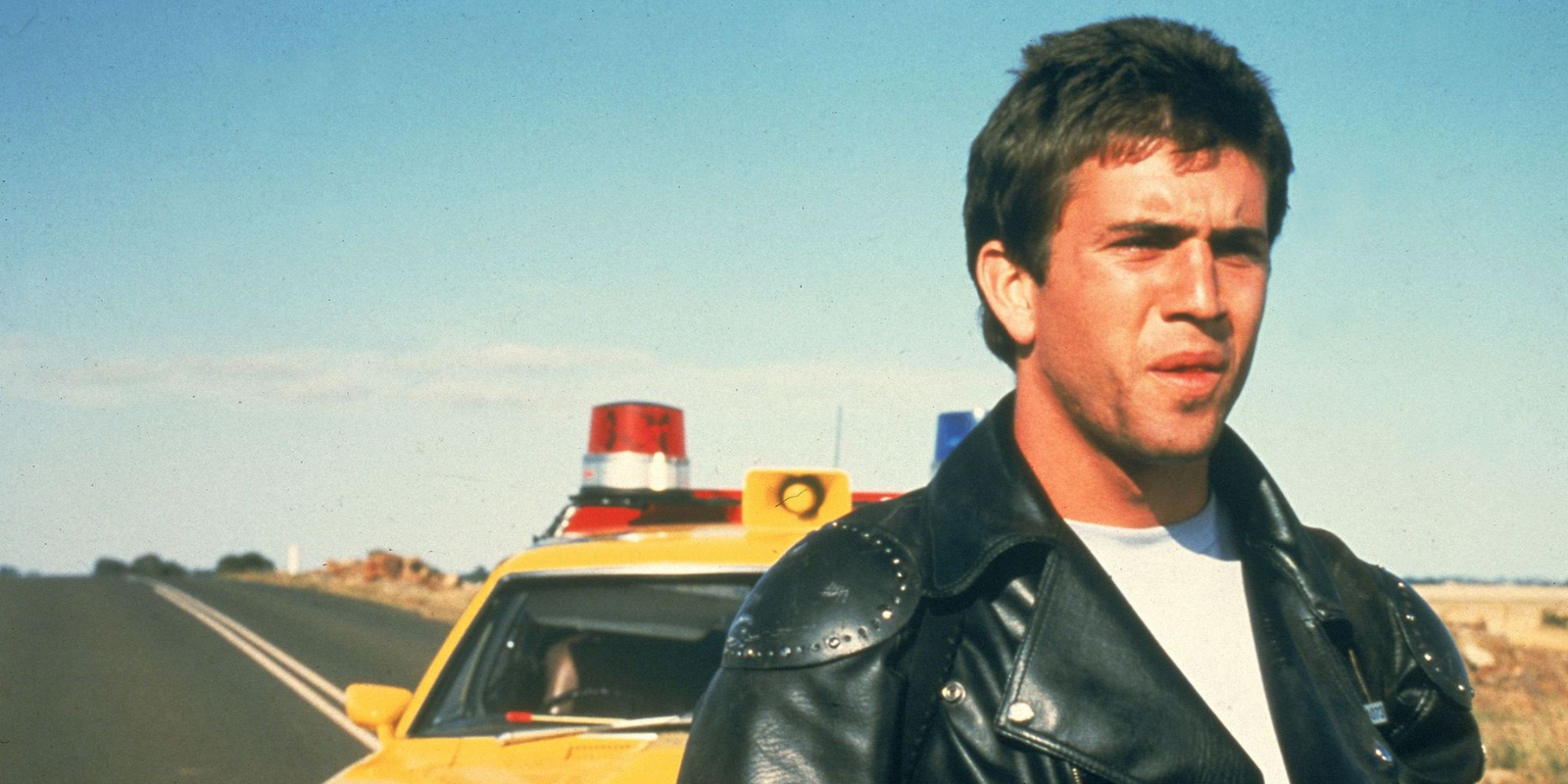 Mel Gibson standing by a yellow car on the highway in in Mad Max