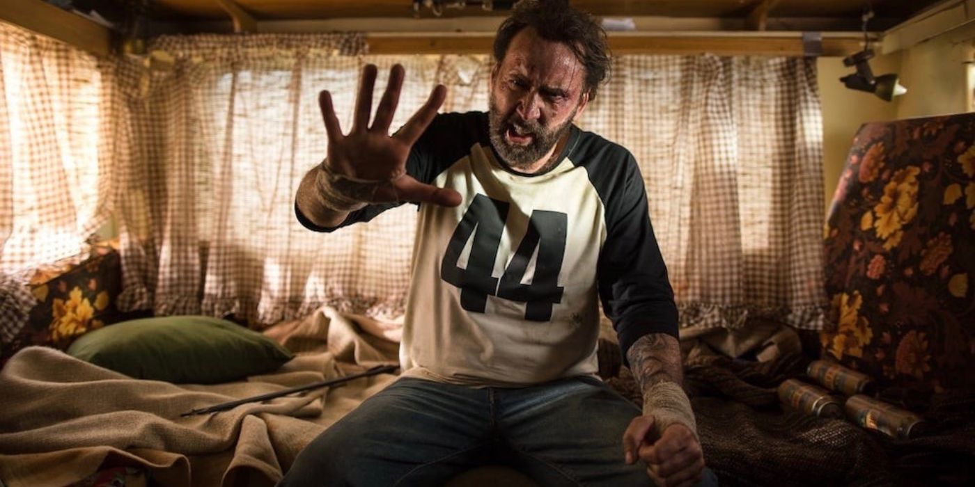 Nicolas Cage como Red sentado em uma cama e segurando a mão em Mandy
