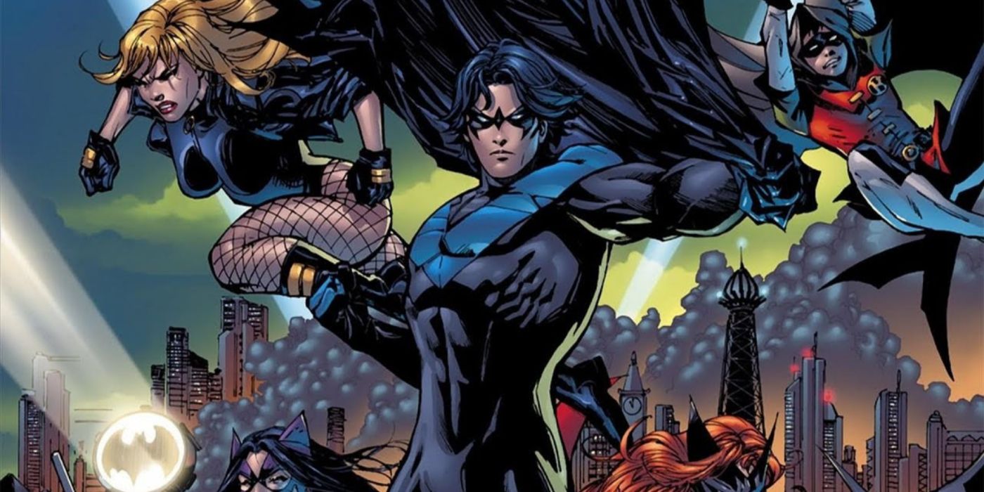 Nightwing holding the cape and cowl of Batman with the supporting family behind him.