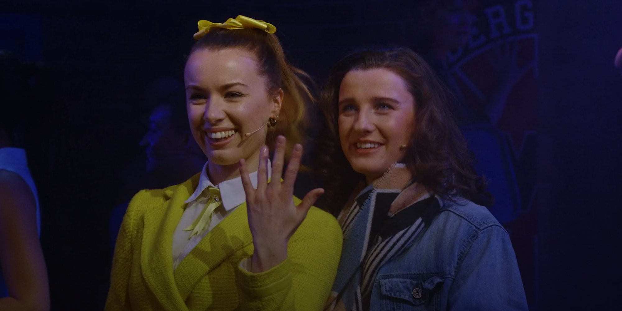 Heather McNamara showing off an imaginary engagement ring beside Veronica in Heathers: The Musical