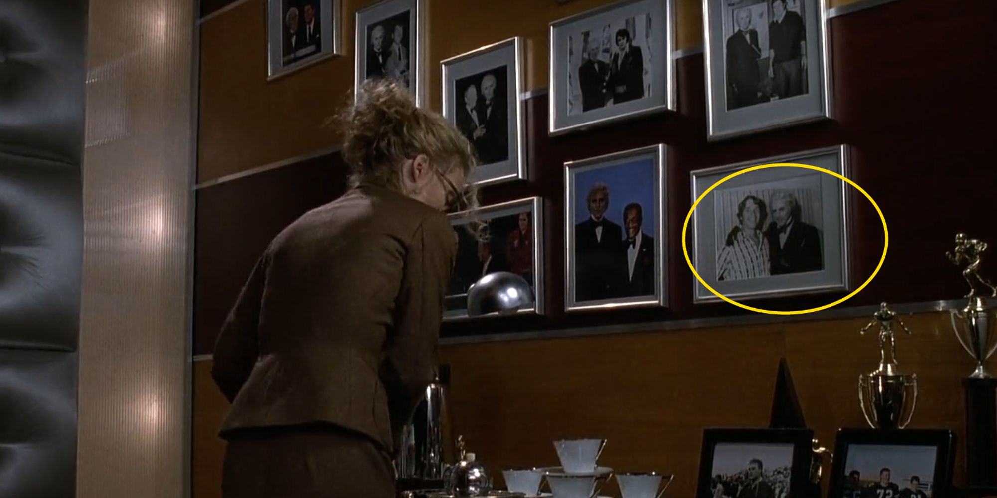 Selina Kyle in front of a wall of Max Shreck's pictures including one with Arnold Schwarzenegger in Batman Returns (1992)