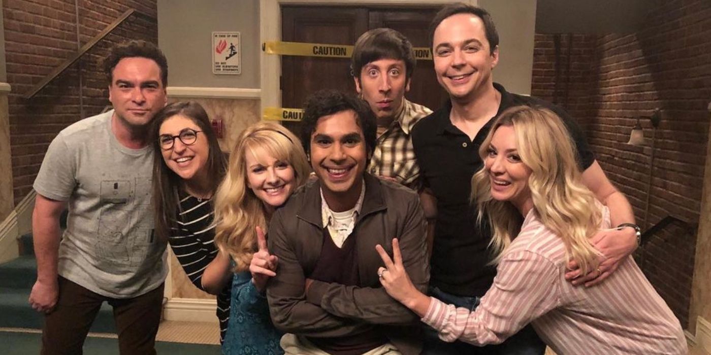 The whole cast of The Big Bang Theory smiling in the hallway between the apartments