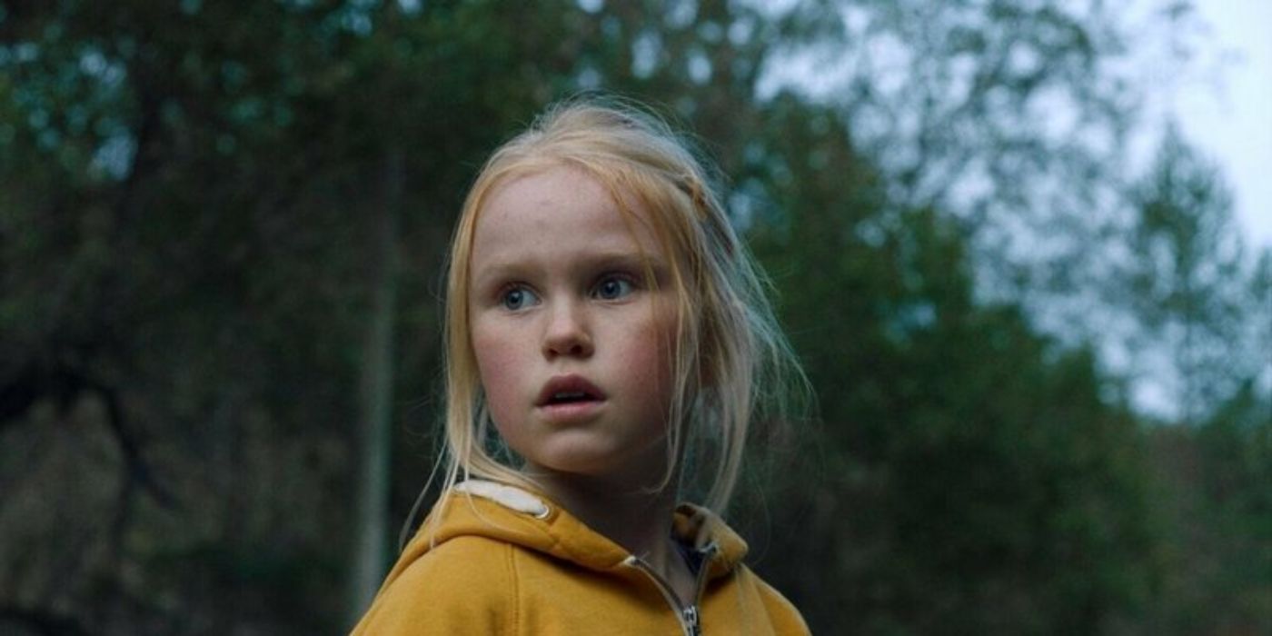 Ida looks back over her shoulder while standing in a wooded area in The Innocents.