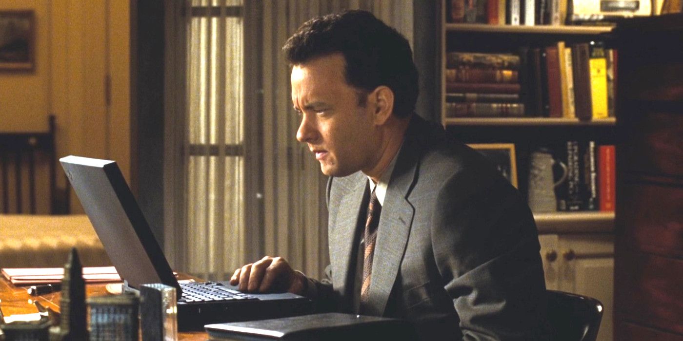 Tom Hanks em You've Got Mail sentado ligeiramente curvado para a frente apertando os olhos para uma tela de laptop