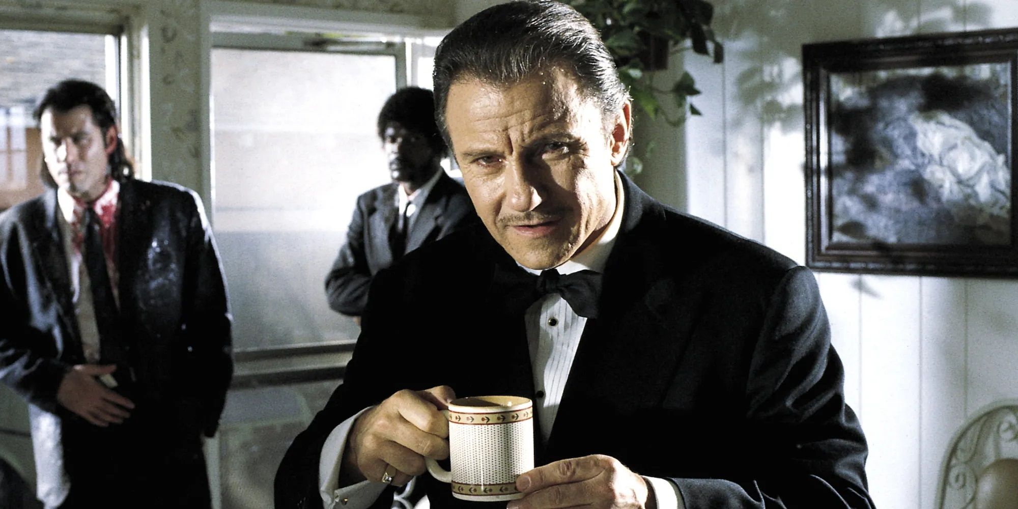 Harvey Keitel as Winston Wolf drinks a coffee (with John Travolta as Vincent Vega and Samuel L. Jackson as Jules in the background) in Pulp Fiction