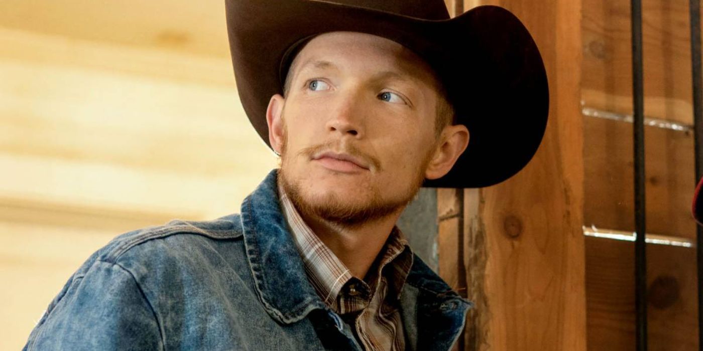 Jefferson White looks to his right while standing against a barn wall in Yellowstones