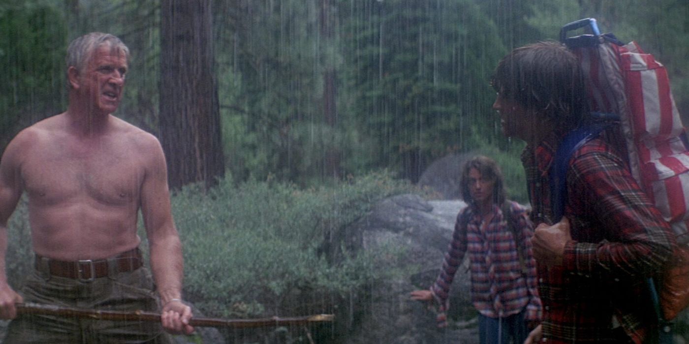 Leslie Nielsen in Day of the animals, shirtless in the rain holding a stick while two hikers look on