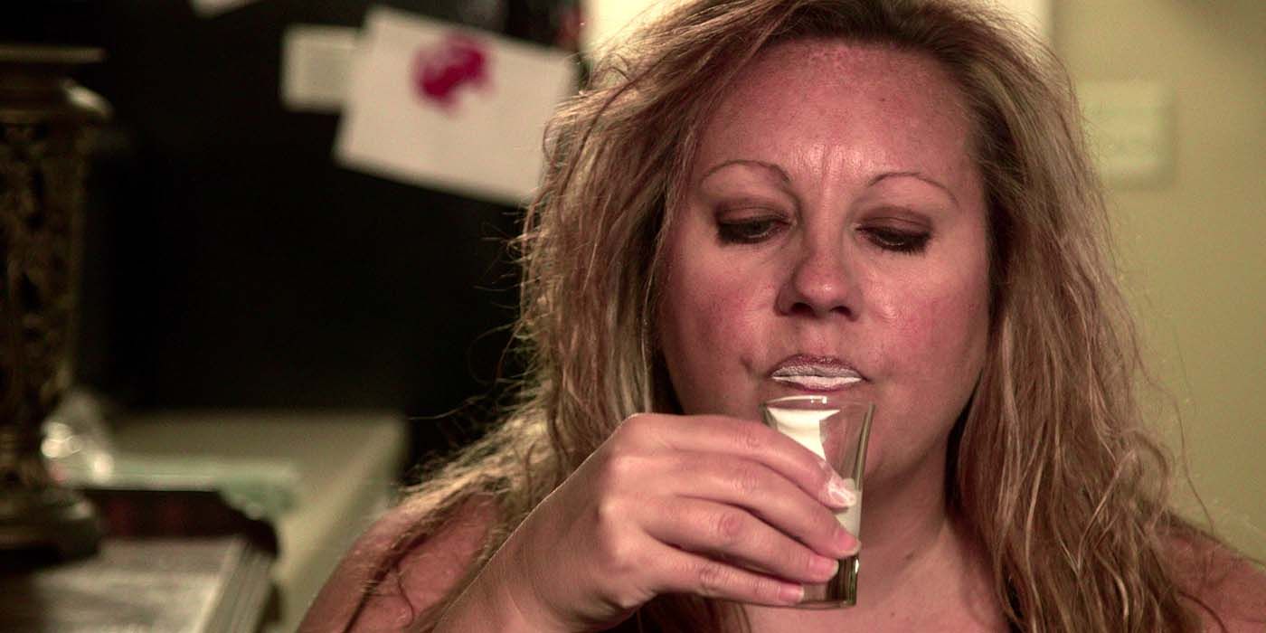 A woman holding a shot glass up to her mouth, looking down into it in a scene from My Strange Addiction.