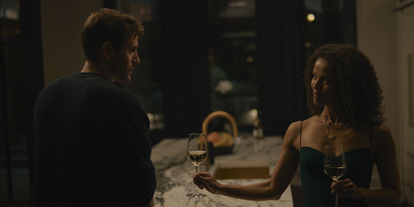Sophie sorrindo, oferecendo a James uma taça de vinho em sua cozinha em uma cena de Surface.