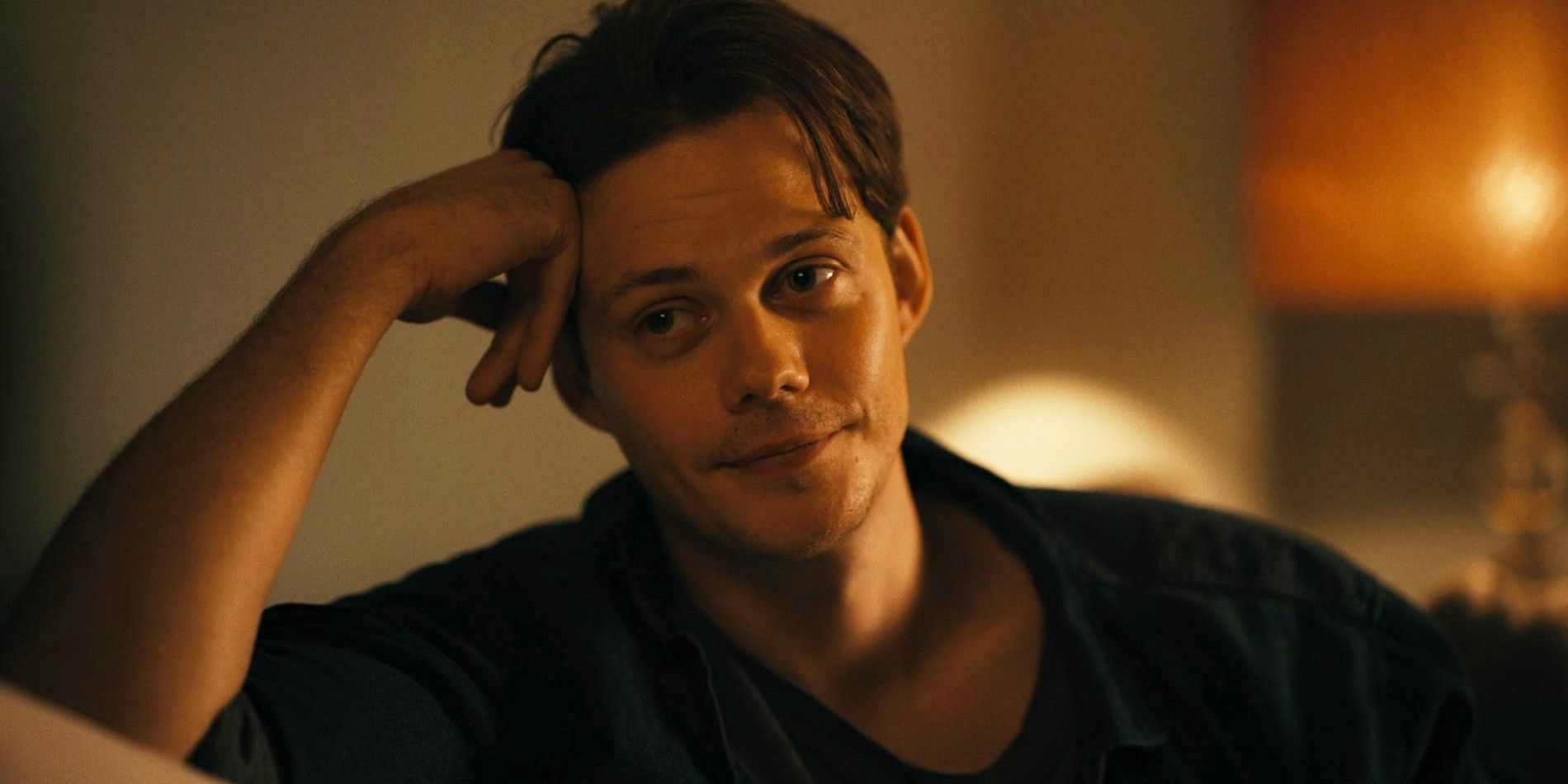 Bill Skarsgard in Barbarian smiling while sitting on the couch