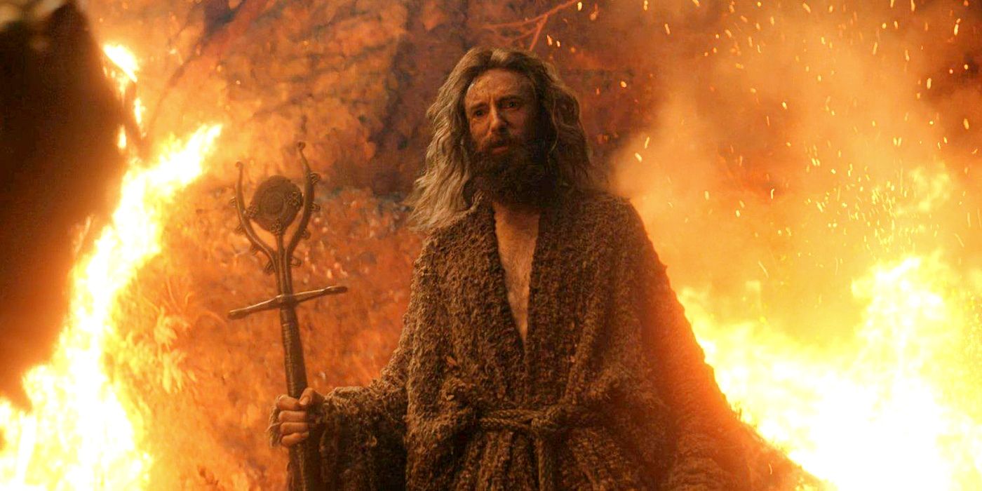 Daniel Weyman as the Stranger holding a staff and standing in front of fire in The Rings of Power