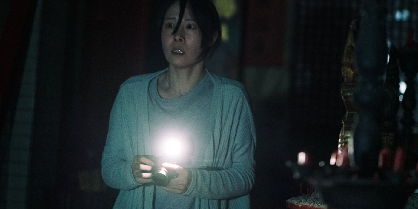 A woman holding a camera with a flashlight in Incantation