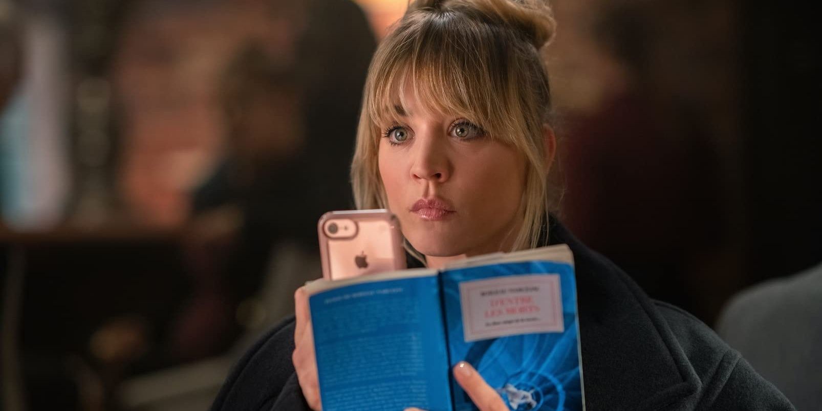 Kaley Cuoco reads a book and holds a phone in The Flight Attendant 