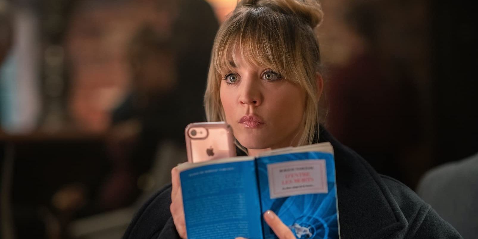 Kaley Cuoco lê um livro e segura um telefone em The Flight Attendant 