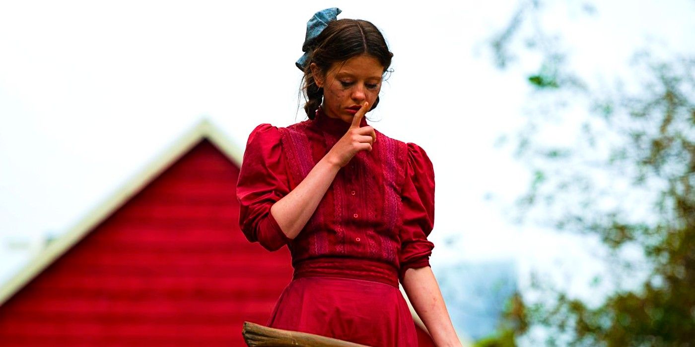 Mia Goth wearing a red dress shushing someone while holding an ax in Pearl