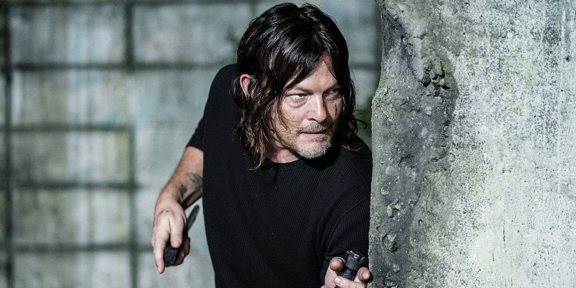 Norman Reedus as Daryl on The Walking Dead season 11 holding knives and peering around a corner