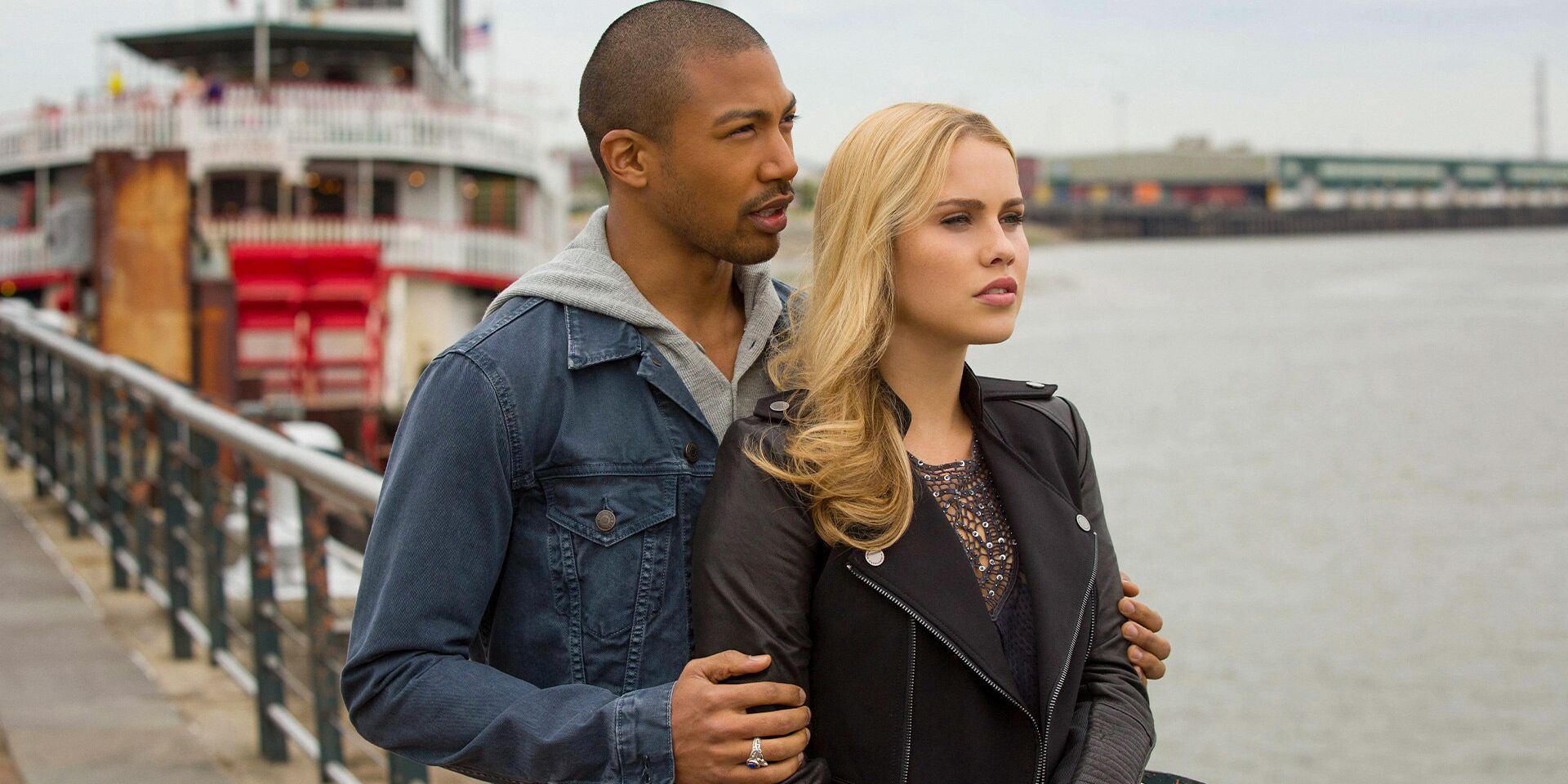 Marcel embracing Rebekah from behind as they stand at the waterfront.