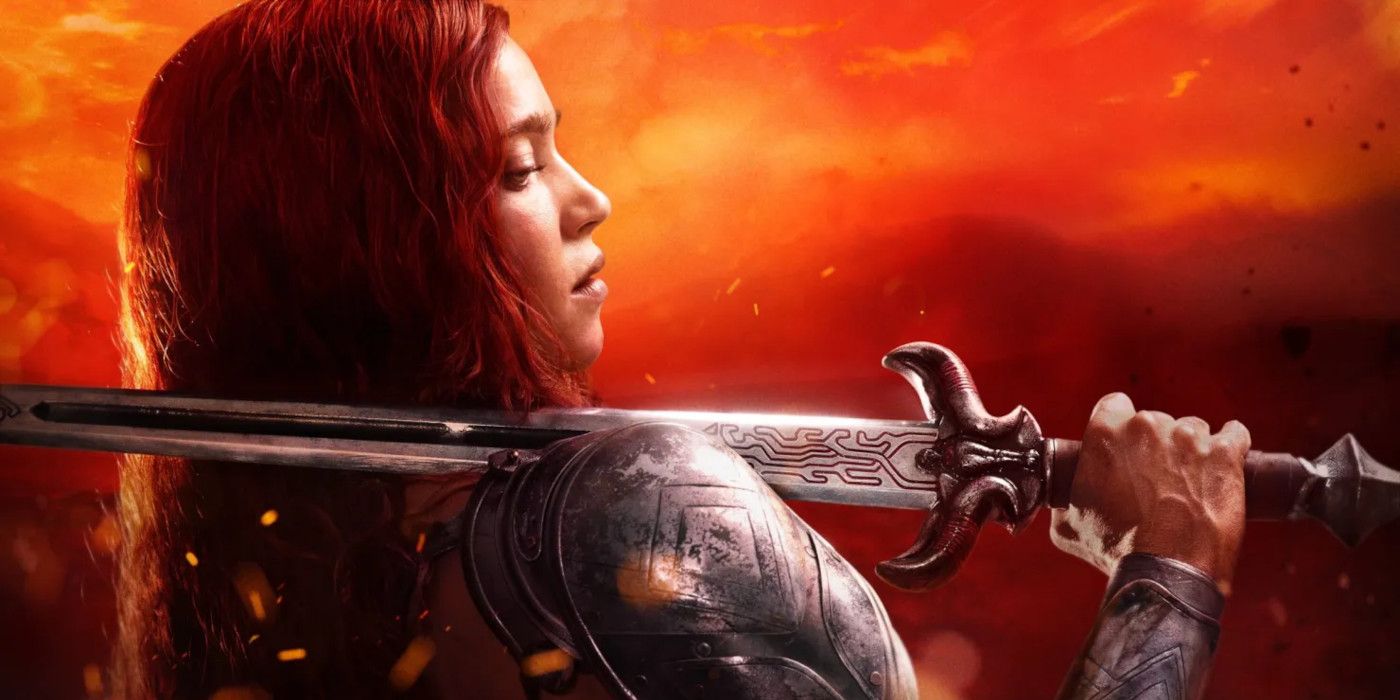 Matilda Lutz as Red Sonja dressed in tarnished armor with a sword slung over her shoulder in front of a fiery backdrop