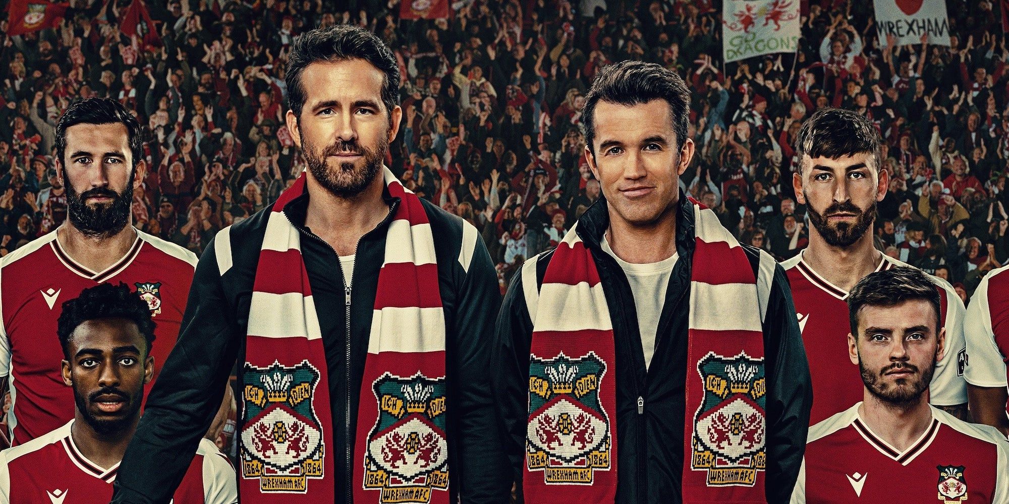 Rob McEllhenny and Ryan Reynolds stand with players in front of a full stadium in Welcome to Wrexham.